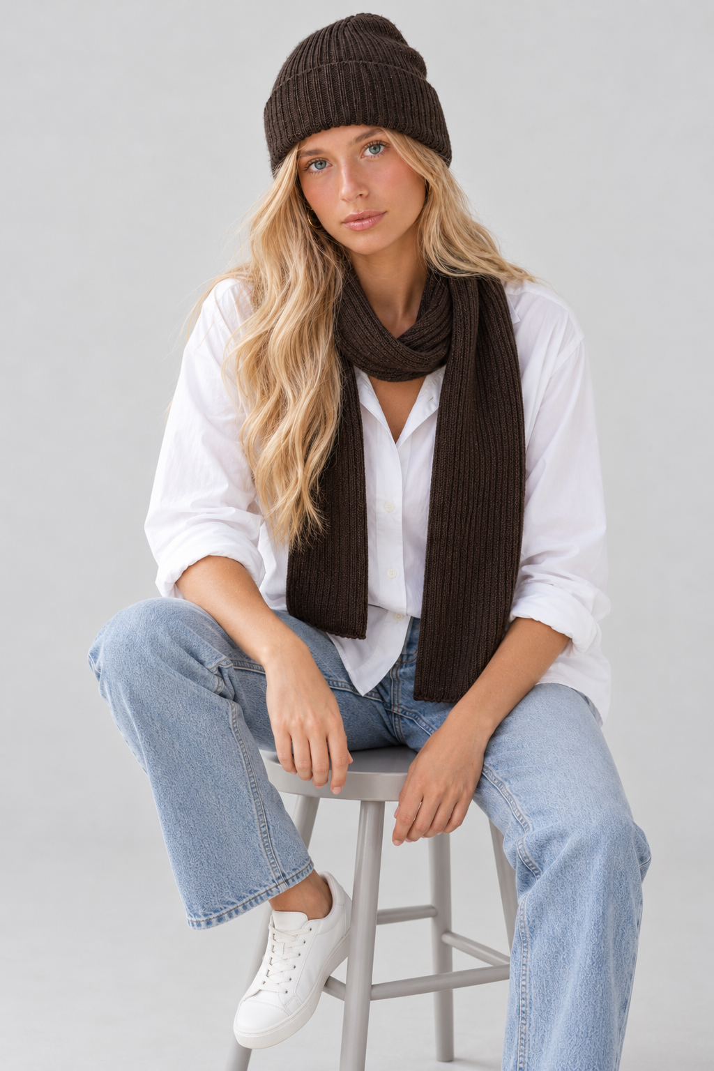Siedząca modelka w komplecie DAILY z wełny merino w kolorze czekoladowego brązu, białej koszuli i jasnych jeansach.