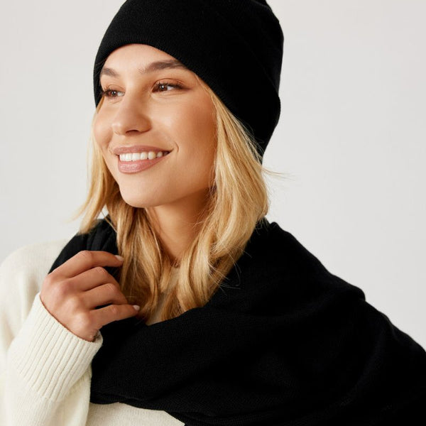 Czapka beanie czarna z wełny merino – stylizacja damska na modelce. Widok z boku uśmiechniętej dziewczyny.