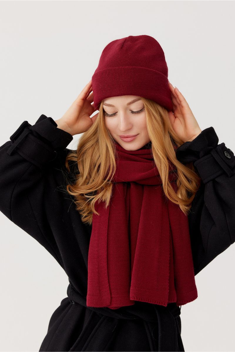szal oversize bordo damski welna merinona modelce która trzyma się za głowę na której też ma czapkę w komplecie w kolorze bordo z merino.