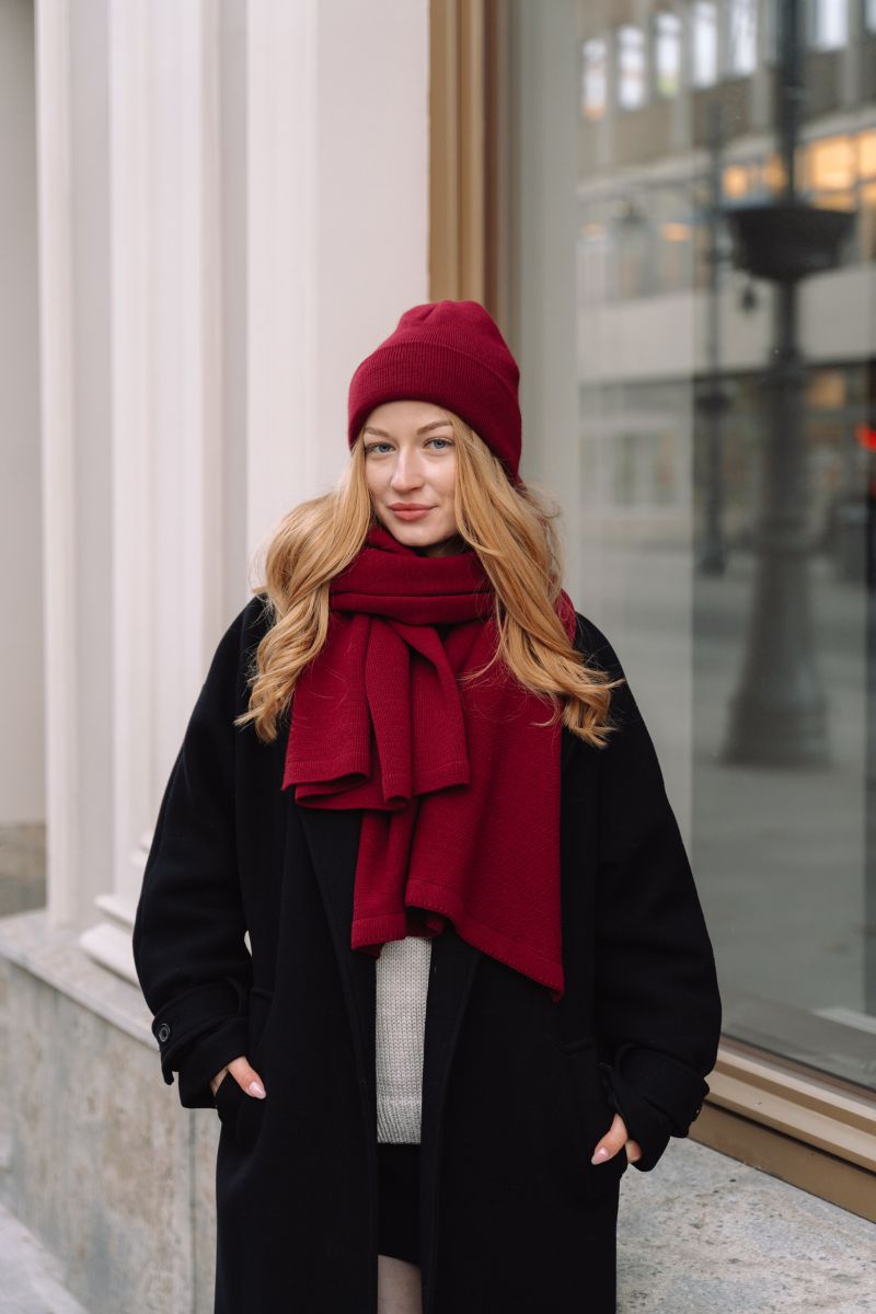 szal penelope bordowy cieply i oddychajacy na modelce która ma czapkę bordo w komplecie w stylizacji w płaszu na ulicy. 